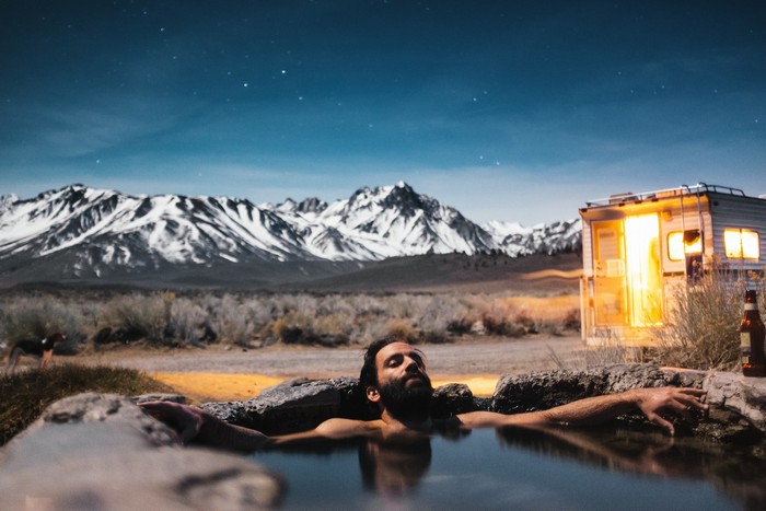Guy relaxing with an RV and snow-capped mountains in the background.